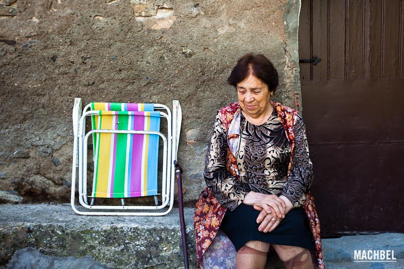 Señora mayor mirando al suelo sentada a la puerta de casa junto su bastón y silla de playa. Montañana, Aragón, España